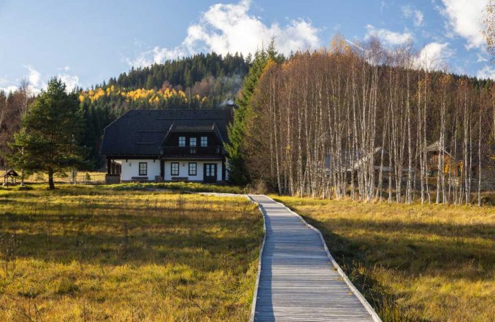 Infocentrum Svinná Lada v pozadí snímku, vepředu je vidět poválkový dřevěný chodnék vedoucí přes travnatý povrch