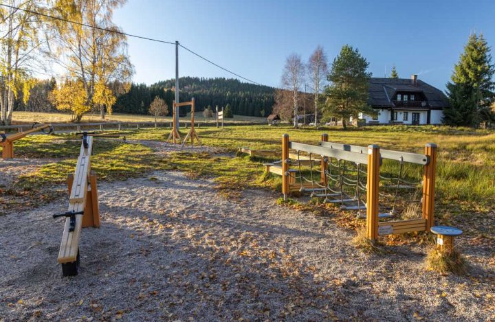 Hřiště u infocentra Svinná Lada, v popředí dřevěné prvky, za nimi je vidět část budovy střediska